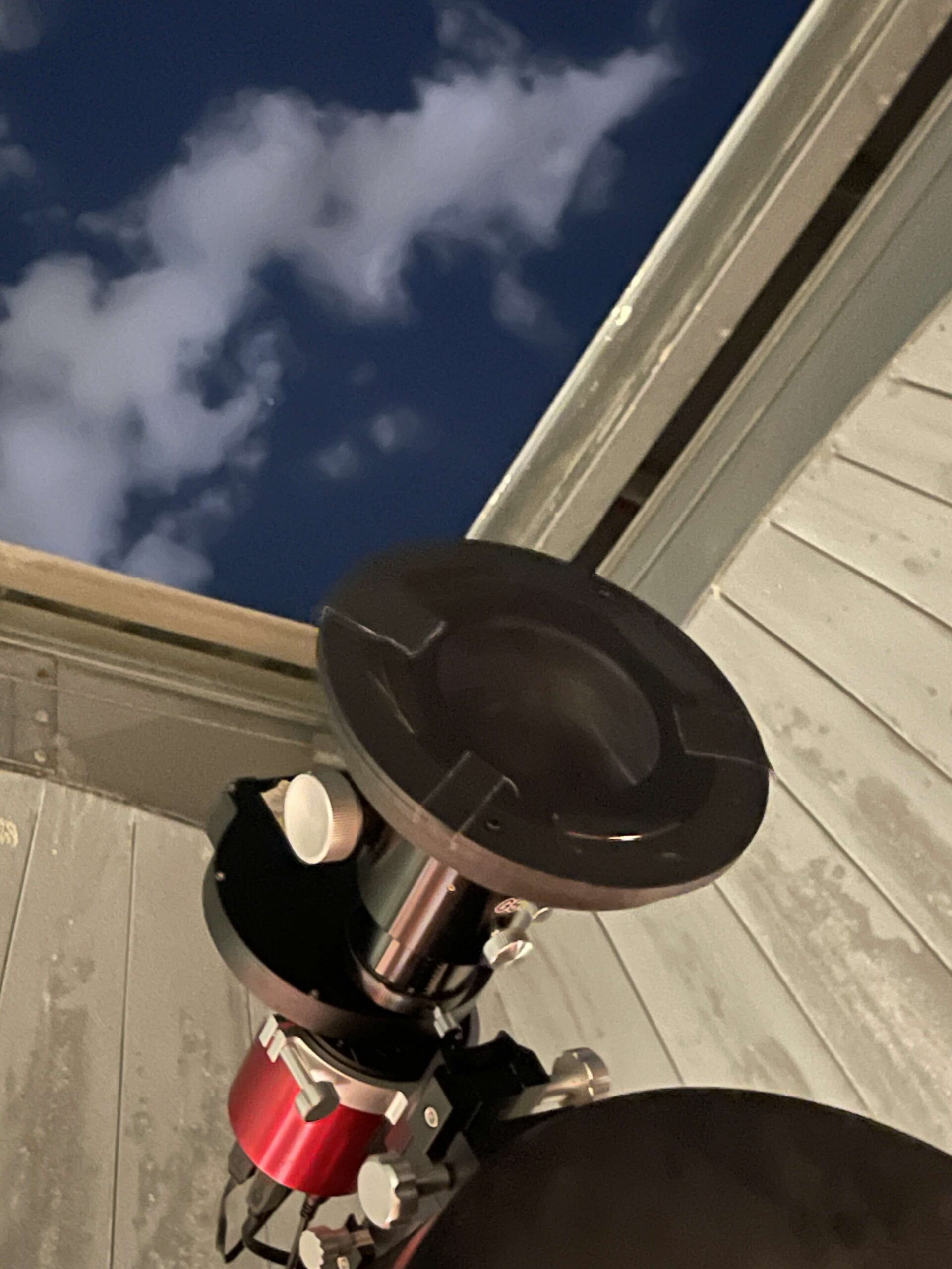 A flat disc lens installed in a microscope with the sky in the background.