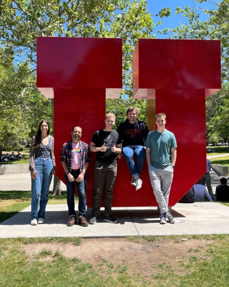 Tanmoy and his mentees standing in front of the University of Utah's logo, a large, red "U."