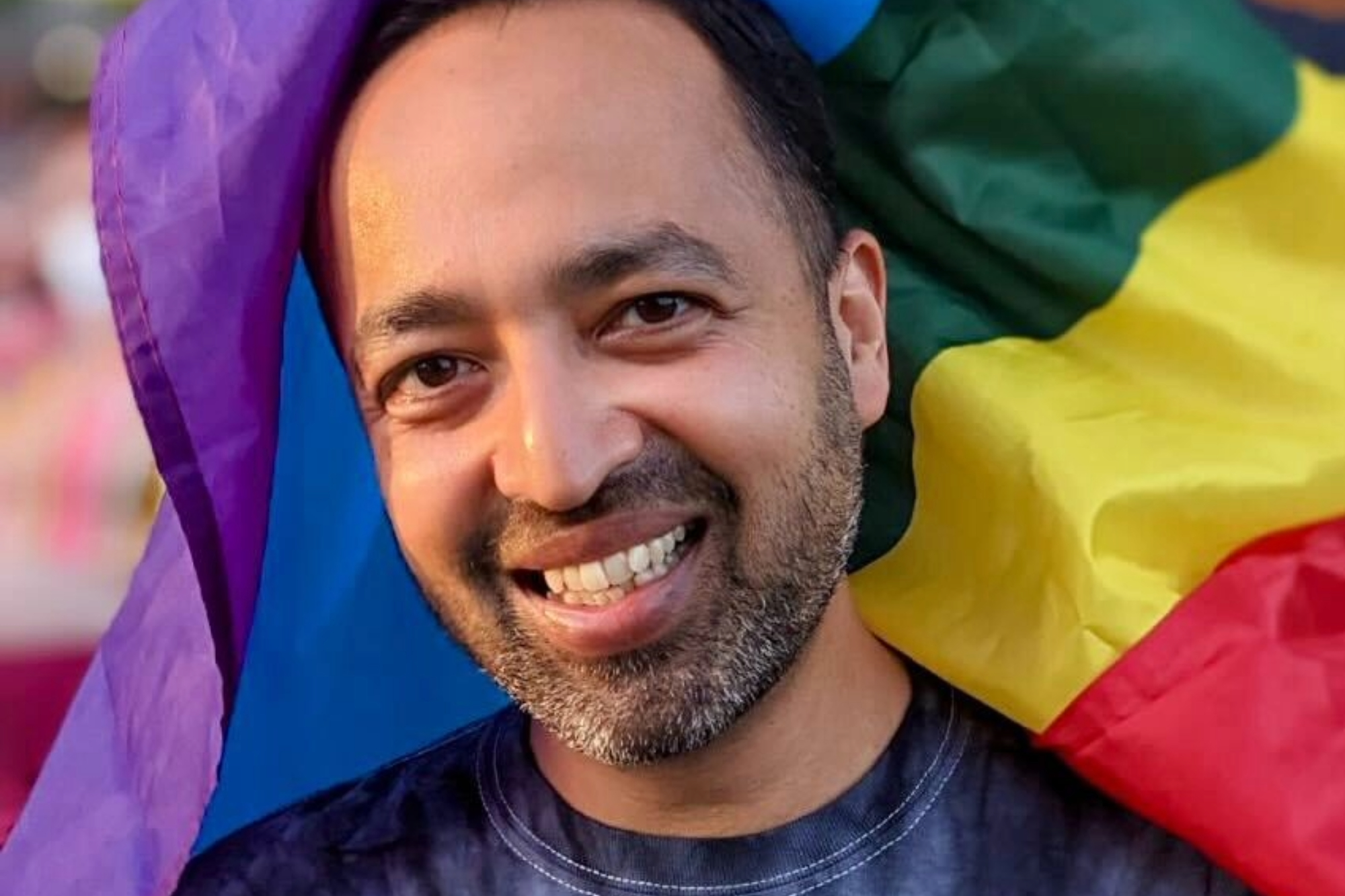 Professor Tanmoy Laskar smiling with a rainbow flag in the background.