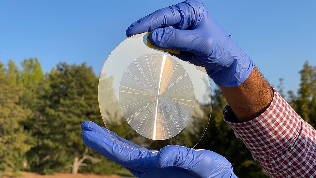 Two gloved hands holding a flat disc lens reflecting sunlight.