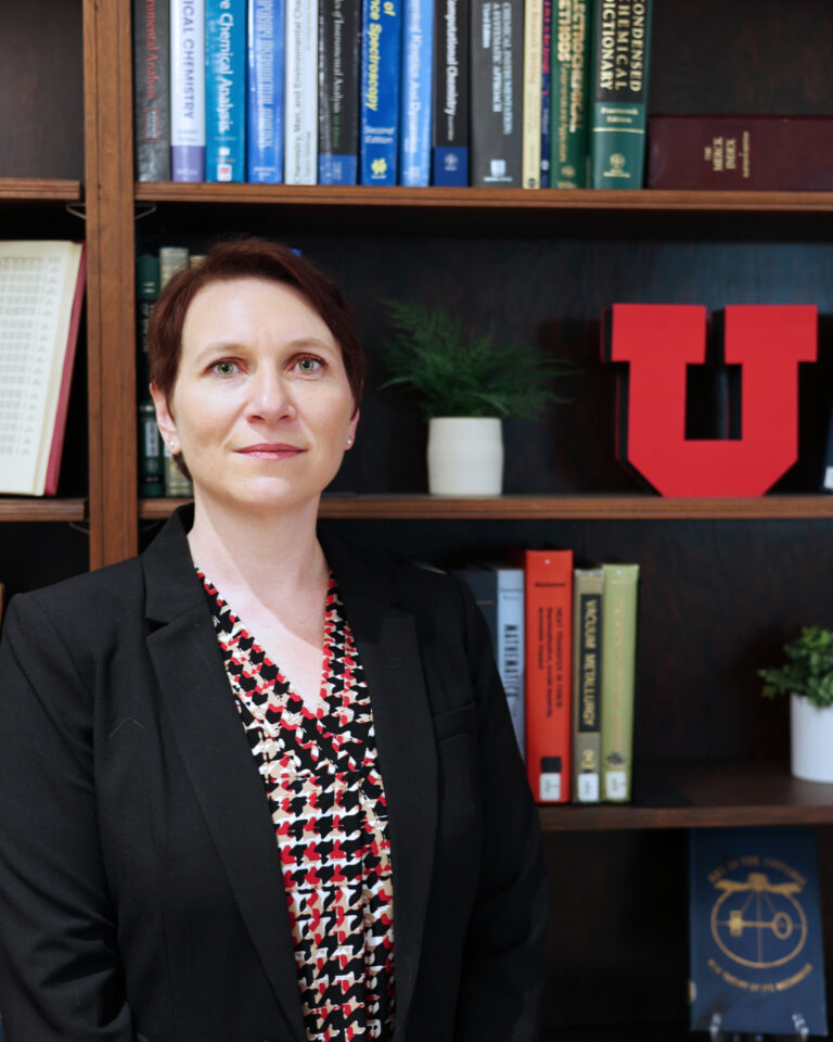 Pearl Sandick standing in front of bookshelves filled with books and a large University of Utah logo.